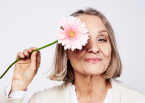 Ältere Frau mit rosa Blume vor dem Auge